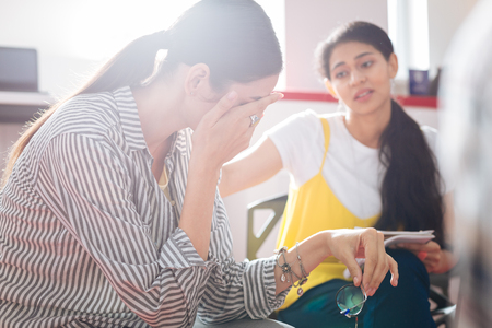 Psychological help. Unhappy stressed woman crying and hiding her face while a professional reliable psychologist looking at herの写真素材