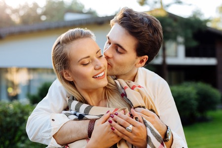 Tender and romantic. Delighted happy woman smiling while enjoying the kiss in the cheekの写真素材