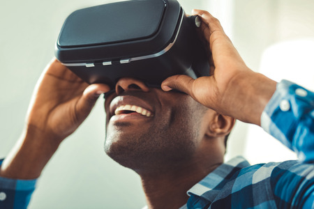 Innovative technologies. Low angle of merry afro american man putting on VR glasses and tuning themの写真素材