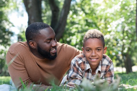 Close to nature. Positive happy boy lying in the grass while being together with his fatherの写真素材