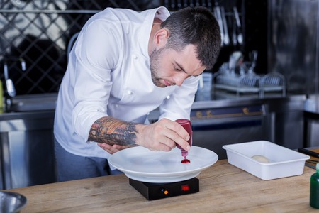 Tattooes. Tatooed cook being attentive while cooking a dishの写真素材