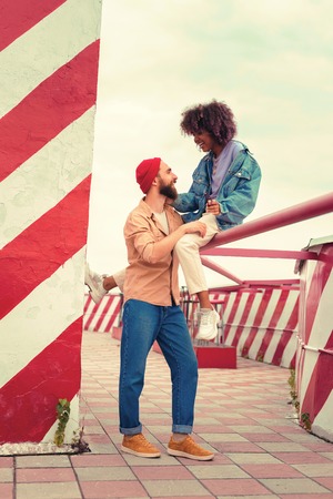 Chatting and smiling. Beautiful young girl smiling and looking at her handsome boyfriend while sitting high and talking to himの写真素材