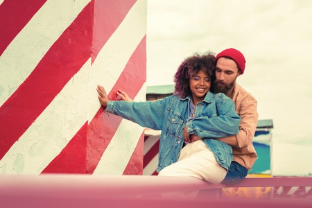Pleasant hug. Beautiful young loving couple sitting on the roof and closing their eyes while huggingの写真素材
