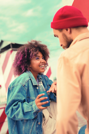 Interesting conversation. Expressive young girl holding blue liquid in glass bottle and smiling while talking to the young manの写真素材