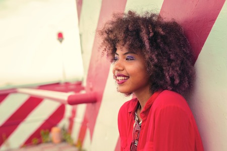 Girl smiling. Laconic portrait of the positive curly young woman standing against the striped wall and smiling happilyの写真素材