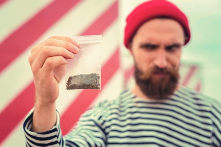 Giving up. Addicted bearded man frowning while looking at the package of tobacco and thinking about giving up smokingの写真素材