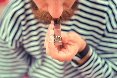 Smoking the pipe. Young bearded man holding tiny metal pipe and smoking tobaccoの写真素材