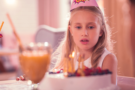 Thoughtful kid. Calm birthday girl thoughtfully looking at the cake and making a wishの写真素材