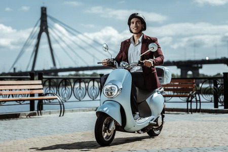 My way. Appealing male student wearing helmet and going on motorbike
