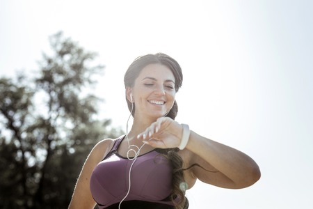 Modern watch. Low angle of a happy nice woman checking the time while looking at her watchの写真素材