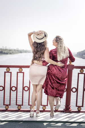Close to nature. Happy delighted women enjoying the beautiful view while standing on the bridgeの写真素材