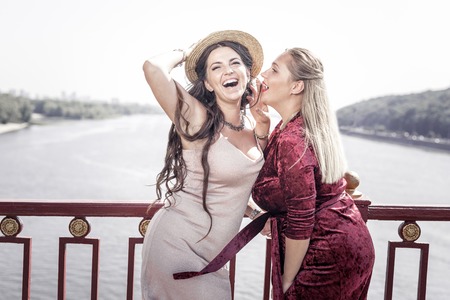 Beautiful location. Positive beautiful woman standing together with her friend on the bridge while...