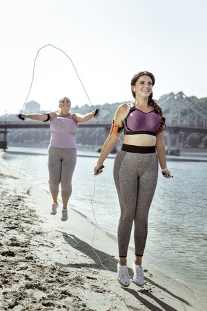 Sports equipment. Delighted nice woman smiling while jumping with a skipping ropeの写真素材