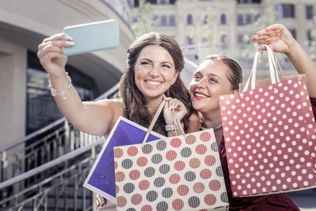 Successful shopping. Happy delighted women showing their bags while taking photos togetherの写真素材