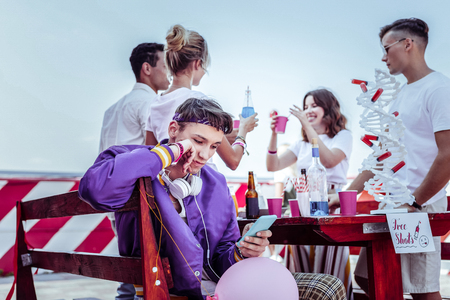 Cocktail party. Attentive boy leaning on bench while looking at telephoneの写真素材