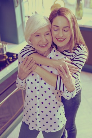 Love in the air. Cheerful young woman keeping eyes closed while embracing her motherの写真素材
