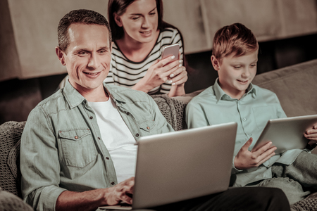 Happy family. Cheerful young people spending time together at home, testing their computersの写真素材