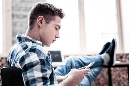 Reading messages. Concentrated young man thoughtfully looking at the screen of his smartphone while reading messagesの写真素材