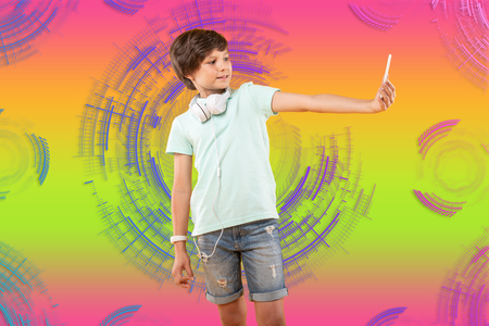 Perfect focus. Confident charming boy taking selfie and posing on colorful backgroundの写真素材