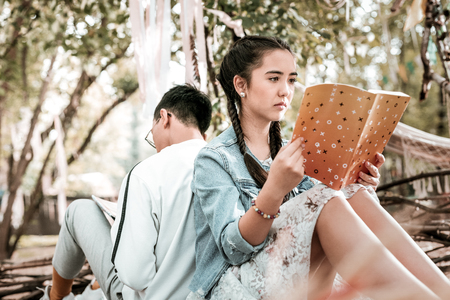 So serious. Delighted brunette holding copybook in both hands and spending her day off in park