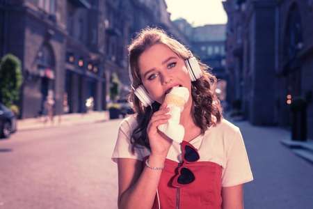 Enjoying taste. Good-looking girl with blue eyes and short dark hair enjoying the amazing taste of delicious ice creamの写真素材