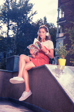 Sneakers and dress. Beautiful girl wearing white sneakers and red summer dress sitting outside enjoying nice warm summer eveningの写真素材