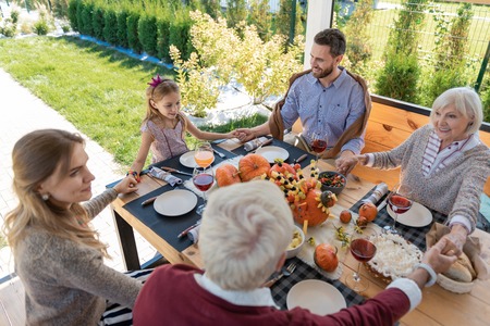 Happy together. Pleased girl sitting in the middle of table and making wishの写真素材