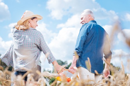 Lovely look. Blonde-haired wife wearing nice beige hat looking at her handsome husband after gathering harvestの写真素材
