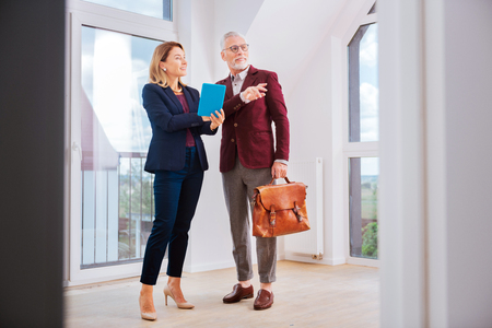 Beautiful agent. Stylish beautiful estate agent wearing blue costume talking to her client while standing in fancy apartmentの写真素材
