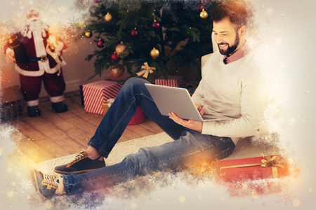 Freelancer on floor. Handsome stylish freelancer sitting on floor near Christmas tree with his laptop while finishing workの写真素材