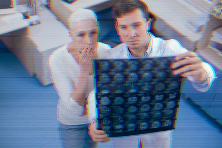 Oh no. Calm young doctor standing with the MRT results in his hands and a senior patient closing her mouth while feeling scaredの写真素材