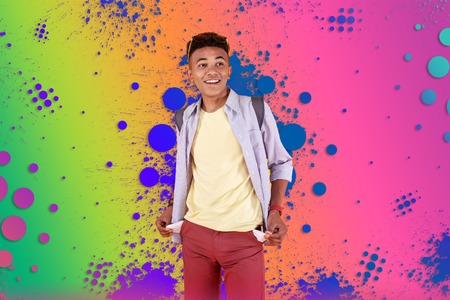 Empty pockets. Stylish mulatto teenager wearing dark red shorts showing his empty pockets while standing in front of colorful backgroundの写真素材