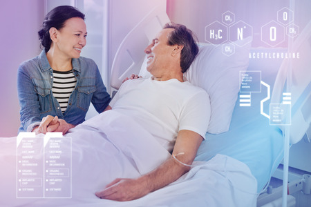 Kind wife. Positive woman supporting her husband and smiling while sitting next to him in a modern hospitalの写真素材