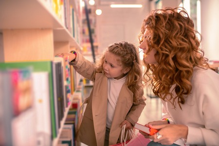 Just take it. Happy curly haired brunette sitting in semi position while looking at booksの写真素材
