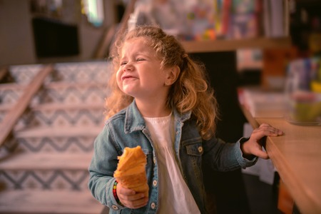 Making face. Cheerful child holding pastry while waiting her mom in cafeの写真素材