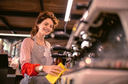 Coffee machine. Pleased female person standing at her workplace while looking downwardsの写真素材
