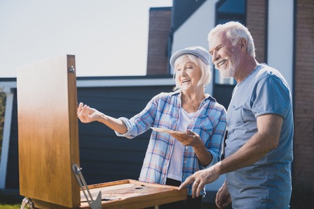 Laughing couple. Elderly happy couple laughing out loud while drawing still life in their garden togetherの写真素材