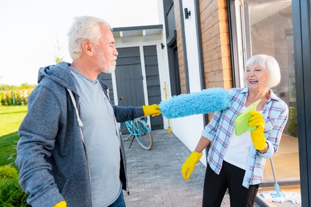 Fun with wife. Bearded grey-haired man having fun with his appealing wife while doing cleaning