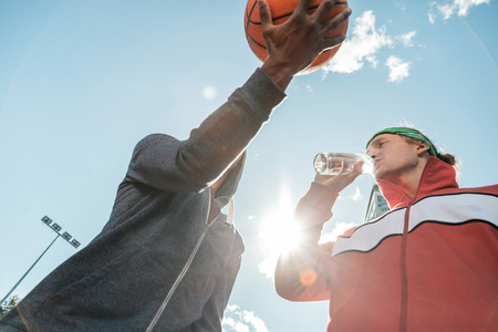 Water balance. Low angle of a pleasant nice man drinking water while talking to his friendの写真素材
