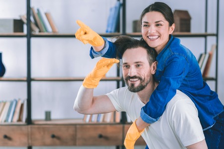 Look in one direction. Happy brunette man keeping his wife on back while raising his right armの写真素材