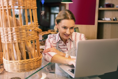 Contacting suppliers. Prosperous owner of bakery using her laptop while contacting suppliers making orderの写真素材
