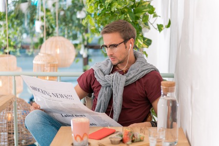 Shocking news. Young handsome entrepreneur wearing glasses reading shocking news while sitting in...