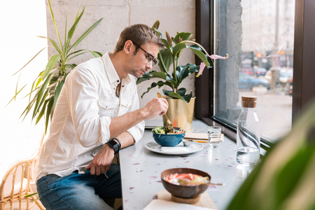 Vegan cafe. Stylish handsome man wearing white shirt feeling relaxed while eating lunch in vegan cafeの写真素材