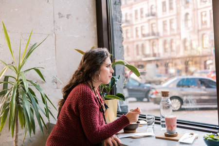Near window. Stylish dark-haired woman wearing nice sweater sitting near window in cafeteriaの写真素材