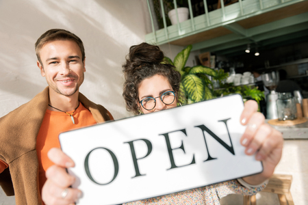 Open sign. Dark-haired woman wearing glasses holding open sign opening cafe with husband