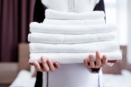 New towels. Selective focus of new white towels being in hands of a nice professional hotel maidの写真素材