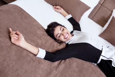 Hotel staff. Top view of an attractive young hotel maid lying on the bed while being in a good moodの写真素材