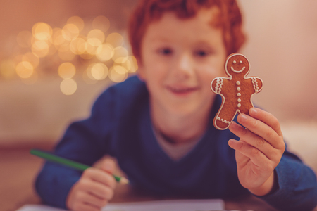 Source of inspiration. The focus being on a gingerbread man in the hands of a cheerful ginger-haired boy drawing him while lying on the floorの写真素材