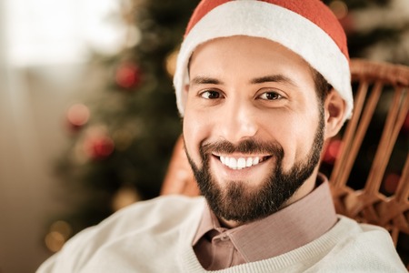 Cheerful smile. Portrait of a happy delighted positive man smiling and looking at you while wearing a Santa hatの写真素材