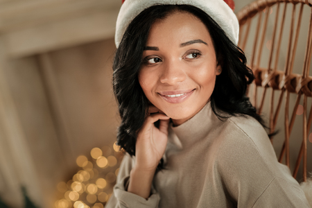 Festive mood. Happy positive dreamy woman smiling and looking aside while wearing a Santa hatの写真素材